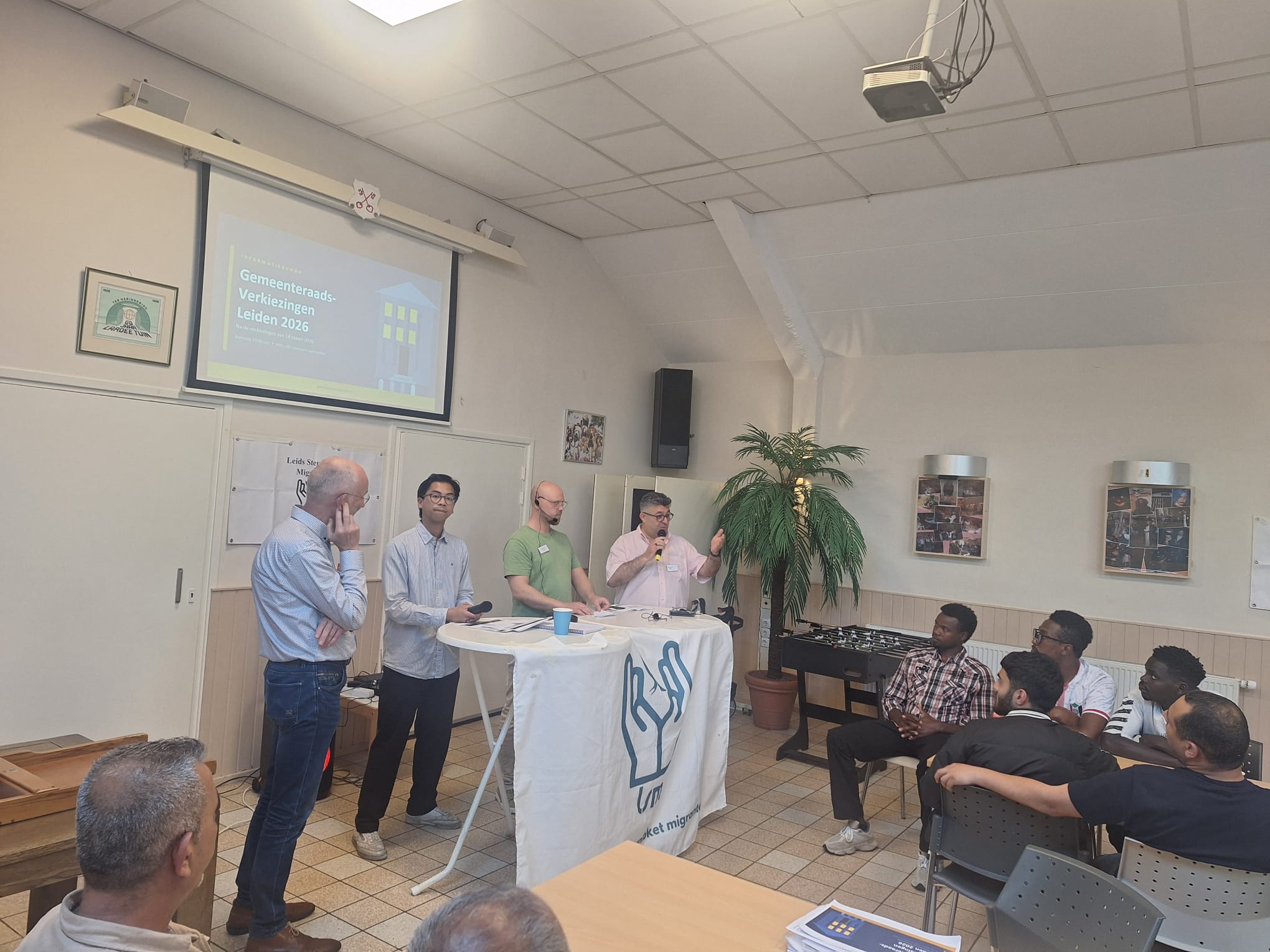Spreekers geven een toespraak tijdens het informatie avond, het publijk kijkt met interesse