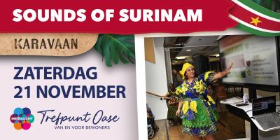 Een vrouw in een kleurrijk Surinaamse jurk wijst naar een scherm met een Surinaamse vlag daarop