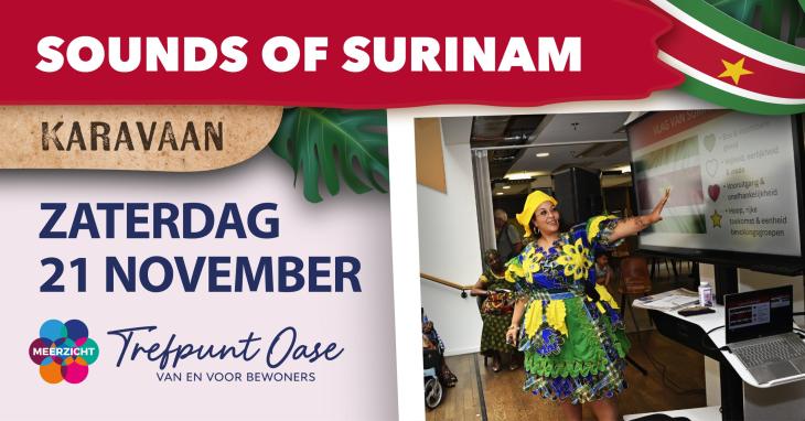 Een vrouw in een kleurrijk Surinaamse jurk wijst naar een scherm met een Surinaamse vlag daarop